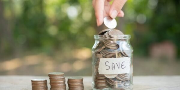Person putting a coin in a jar filled with coins bearing the label "Save"