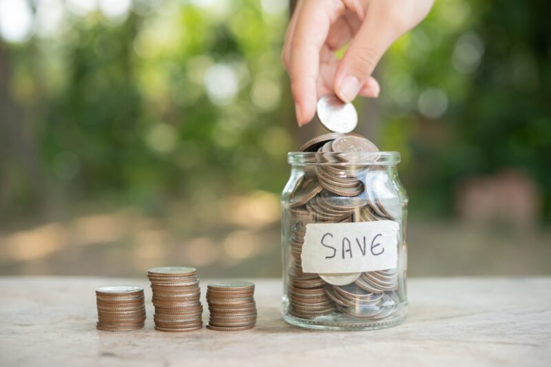 Person putting a coin in a jar filled with coins bearing the label "Save"